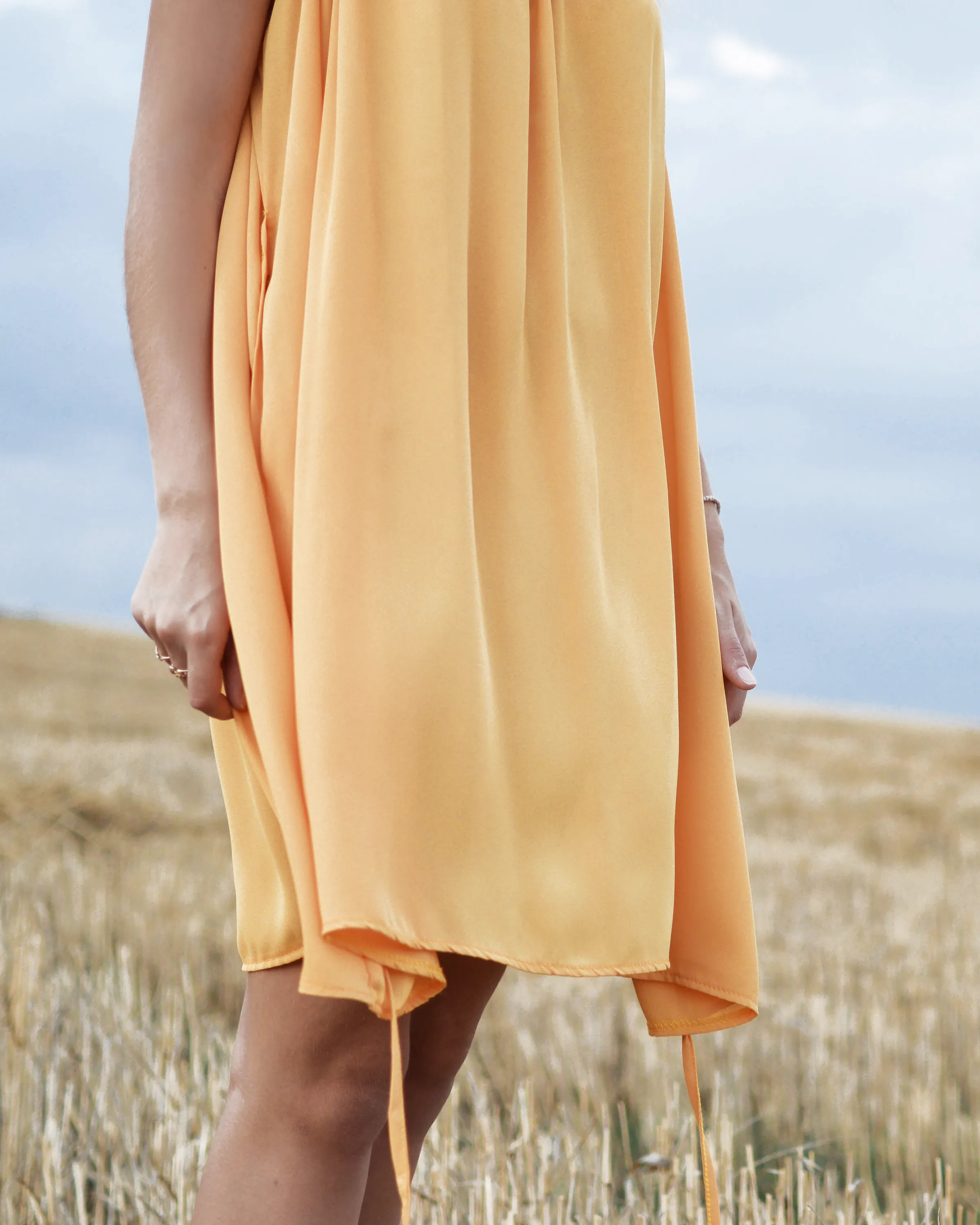 The saffron Sahrami silk dress in a stubble field.