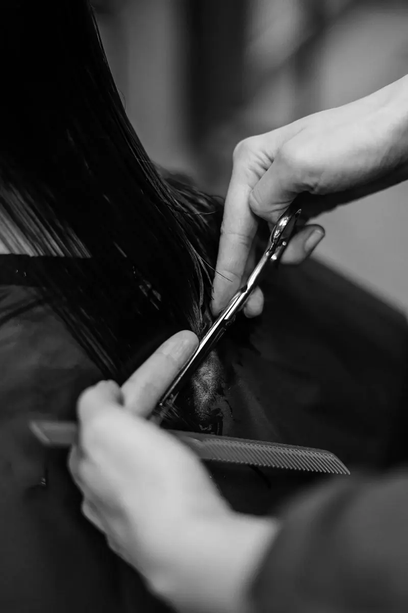 A stylist cutting dark hair with scissors and a comb