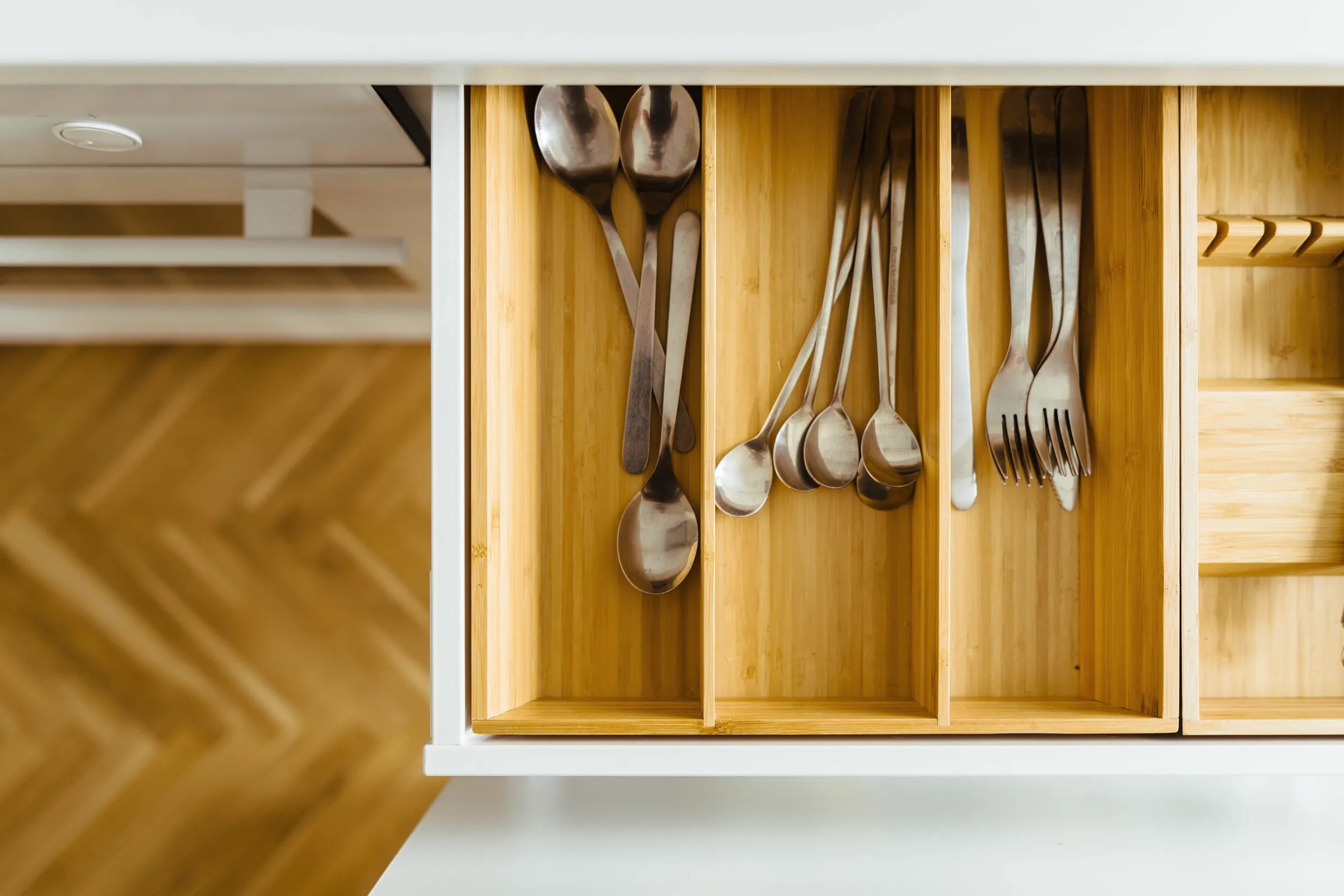 An open drawer with wooden dividers above a herringbone floor.