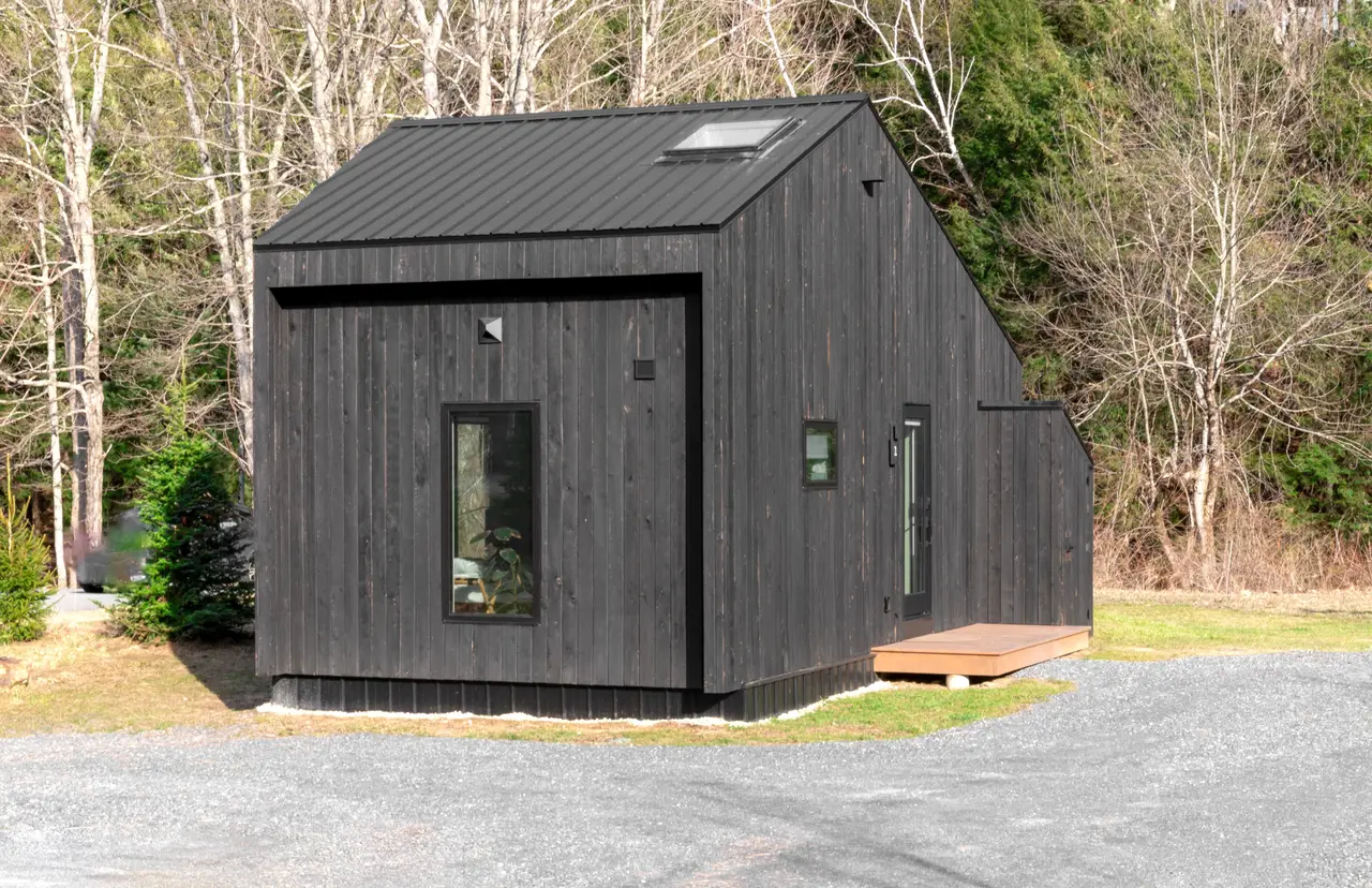 A finished small house clad in black vertical boards among birch and spruce