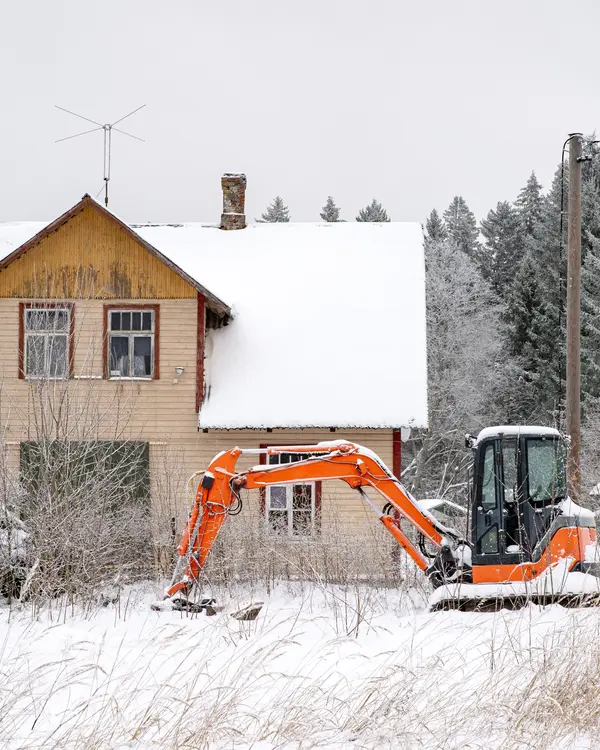 An old wooden house in snow, a small digger in the yard