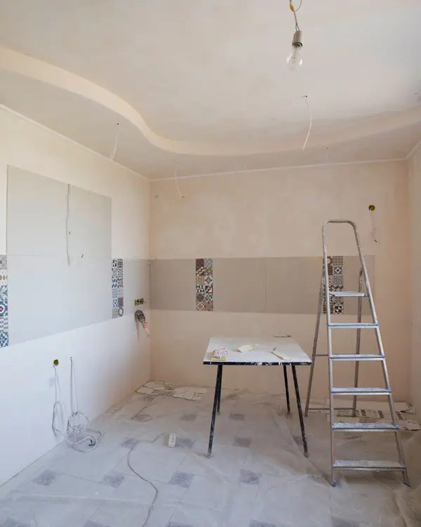A kitchen stripped bare, walls skimmed and tile samples on the wall