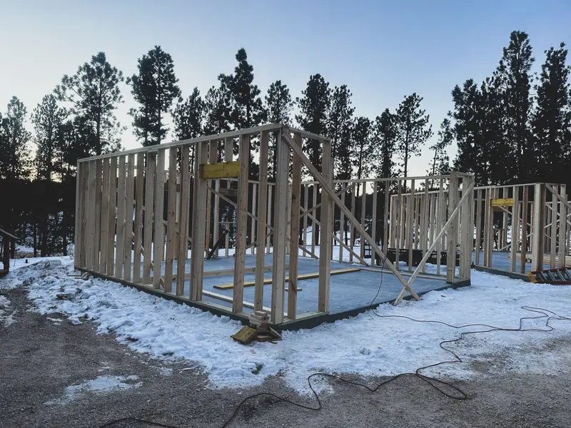 The wall frames of a new house on a snowy plot, pines behind