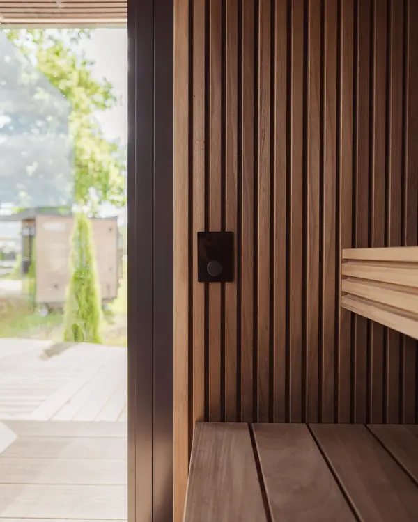A dark wooden sauna, benches and a glass door to the garden
